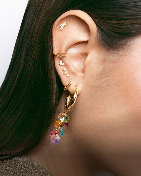 Una oreja de mujer mostrando varios pendientes pequeños y uno largo de colores